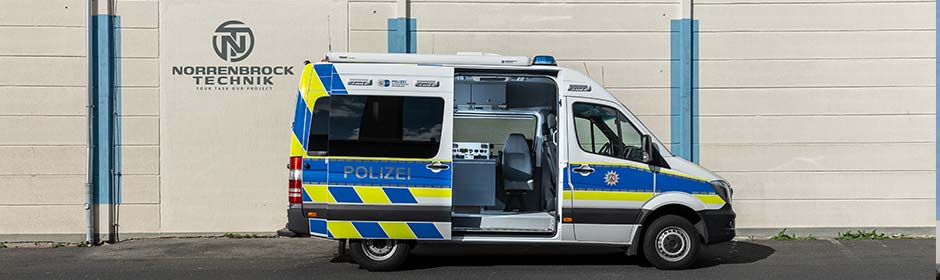 Polizeifahrzeug mit geöffneten Schiebetüren und sichtbaren Arbeitsplätzen vor Wand mit Firmenlogo von Norrenbrock Technik