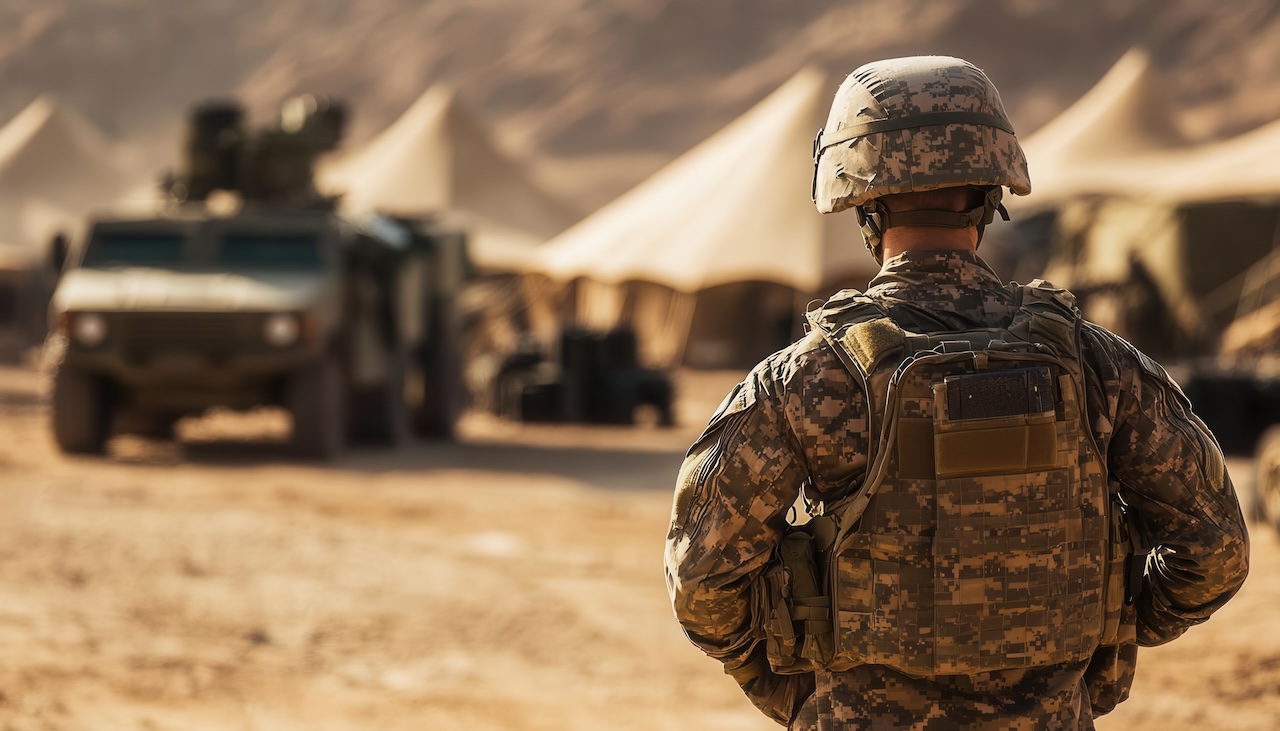 A soldier stands guard near military tents and vehicles in a desert environment, showcasing the essence of military readiness.